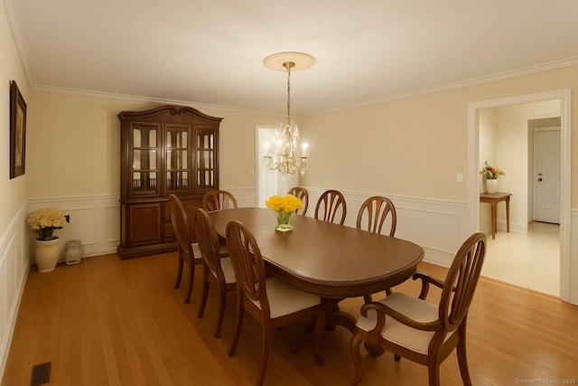 dining space with a chandelier, a decorative wall, crown molding, light wood-type flooring, and a wainscoted wall