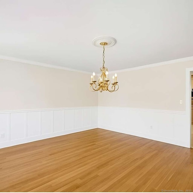 empty room featuring a wainscoted wall, a chandelier, crown molding, and light wood-style floors