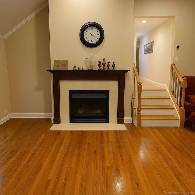 living room featuring crown molding, a tiled fireplace, wood finished floors, baseboards, and stairway