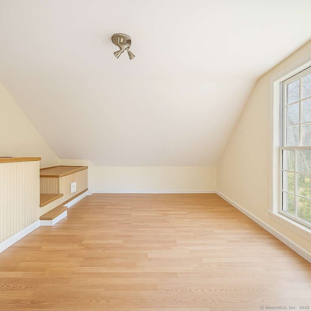 additional living space featuring lofted ceiling, light wood-type flooring, plenty of natural light, and baseboards