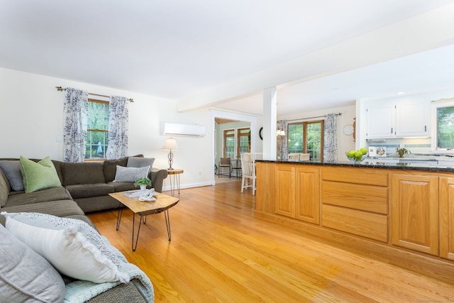 living area featuring a wall mounted AC, light wood finished floors, healthy amount of natural light, and baseboards