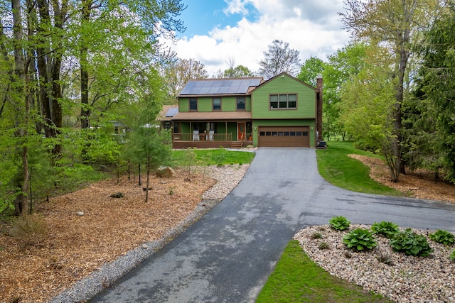 view of front of home featuring covered porch, roof mounted solar panels, driveway, a chimney, and a garage