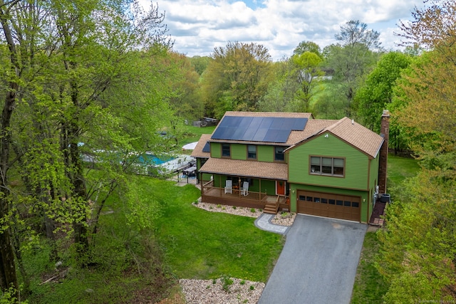 view of front facade featuring covered porch, an attached garage, a front lawn, driveway, and roof mounted solar panels