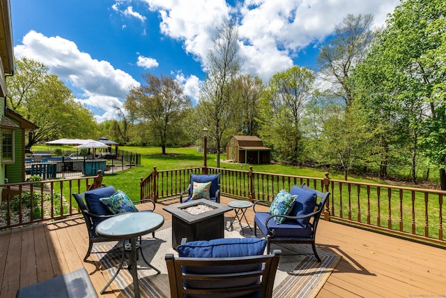 deck with an outdoor fire pit, a lawn, an outbuilding, view of scattered trees, and a storage shed