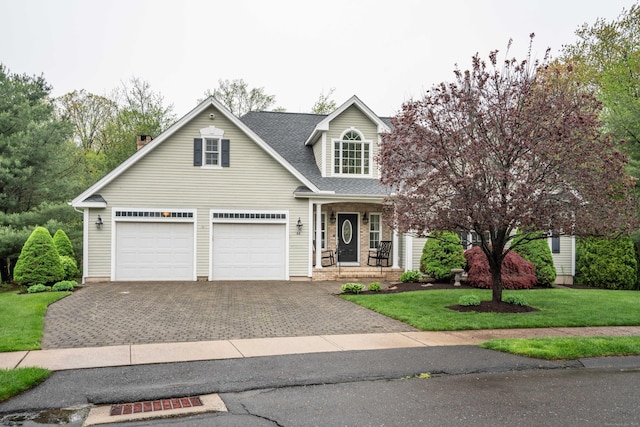view of front facade featuring driveway, a front yard, a shingled roof, and covered porch