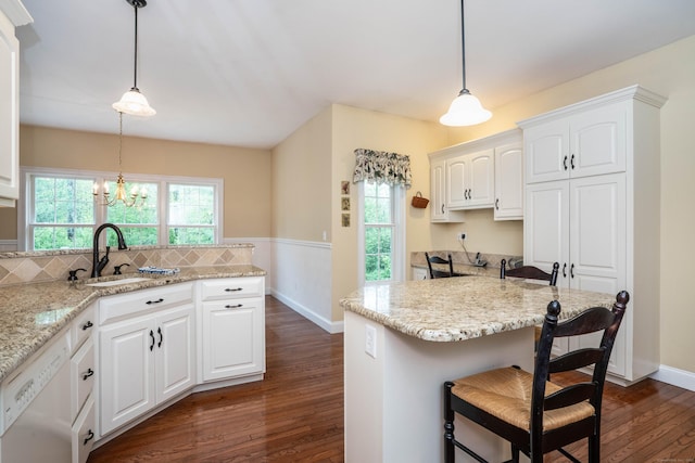 kitchen with dishwasher, a sink, a kitchen breakfast bar, dark wood finished floors, and white cabinets
