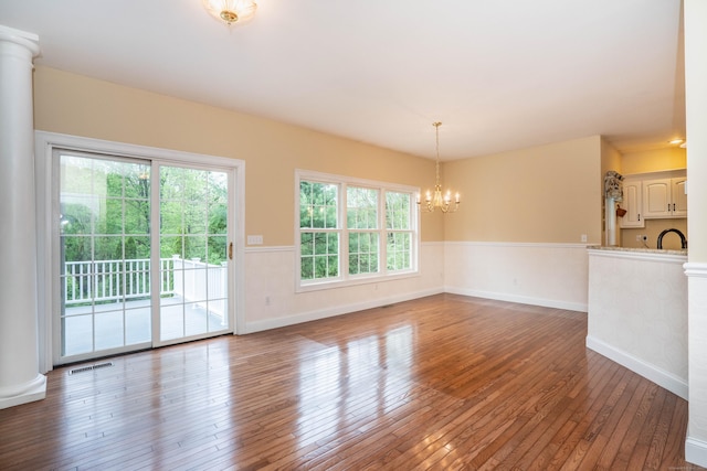 unfurnished room featuring healthy amount of natural light, wood-type flooring, a chandelier, wainscoting, and baseboards