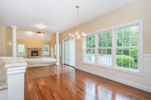 unfurnished living room with hardwood / wood-style flooring, decorative columns, a fireplace, a chandelier, and vaulted ceiling
