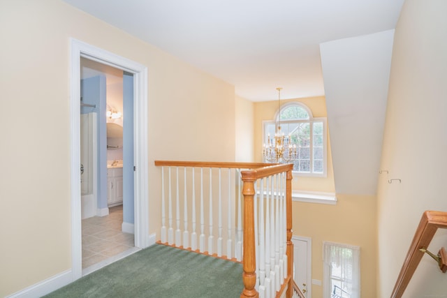 hall with an upstairs landing, a chandelier, carpet flooring, baseboards, and tile patterned flooring
