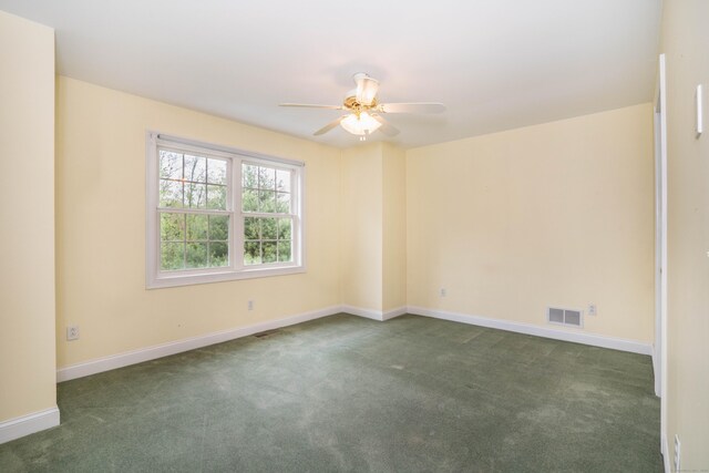 empty room featuring dark colored carpet, ceiling fan, and baseboards