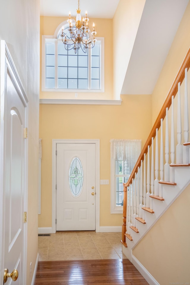 foyer with a chandelier, plenty of natural light, hardwood / wood-style flooring, baseboards, and a high ceiling