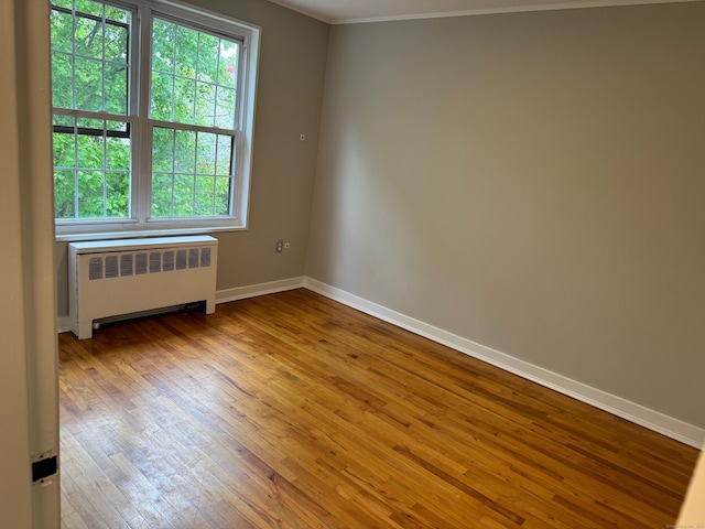 spare room featuring radiator heating unit, hardwood / wood-style floors, baseboards, and ornamental molding