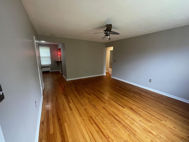 spare room featuring a ceiling fan, wood-type flooring, baseboards, and radiator