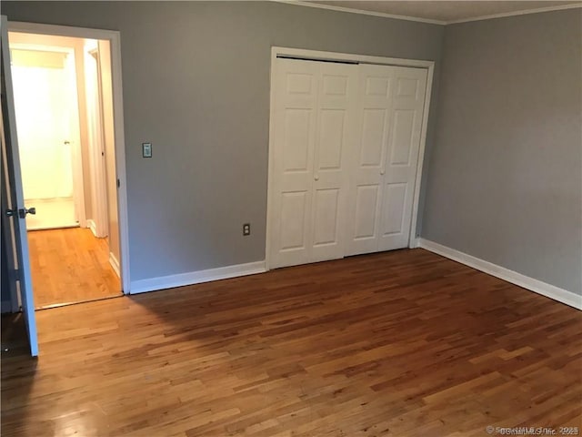 unfurnished bedroom with crown molding, wood finished floors, baseboards, and a closet