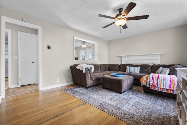 living area with ceiling fan, wood finished floors, baseboards, and a textured ceiling