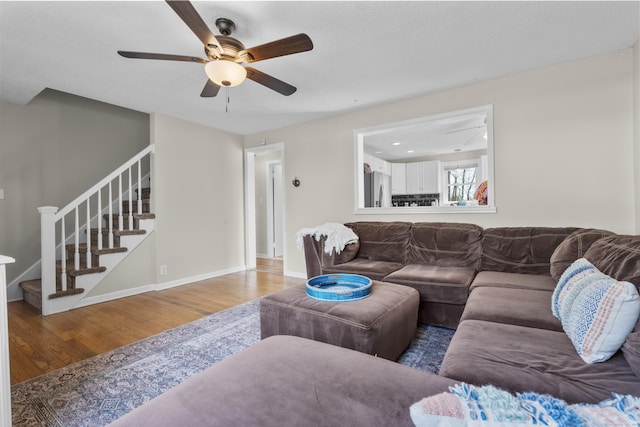 living room featuring wood finished floors, ceiling fan, stairway, and baseboards