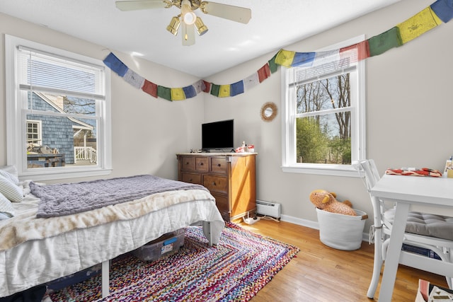 bedroom featuring a baseboard heating unit, multiple windows, wood finished floors, and baseboards