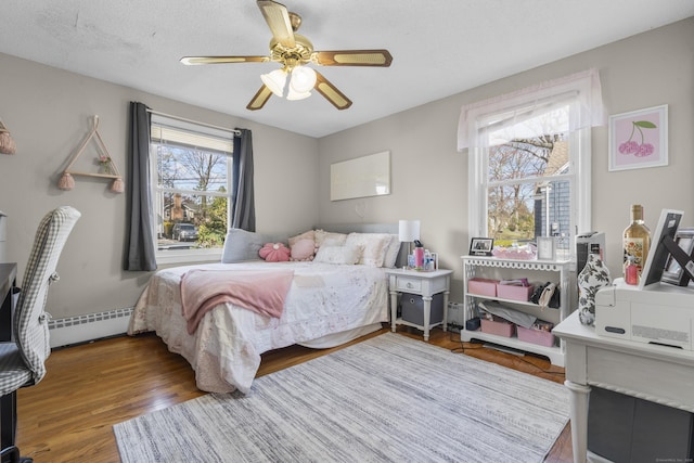 bedroom with a baseboard heating unit, wood finished floors, and ceiling fan
