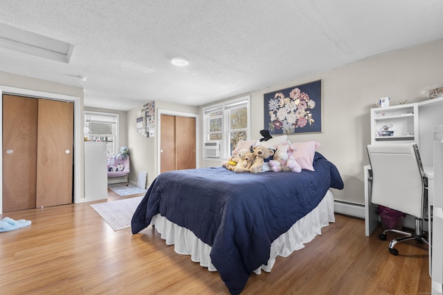 bedroom featuring two closets, light wood finished floors, a textured ceiling, baseboard heating, and attic access