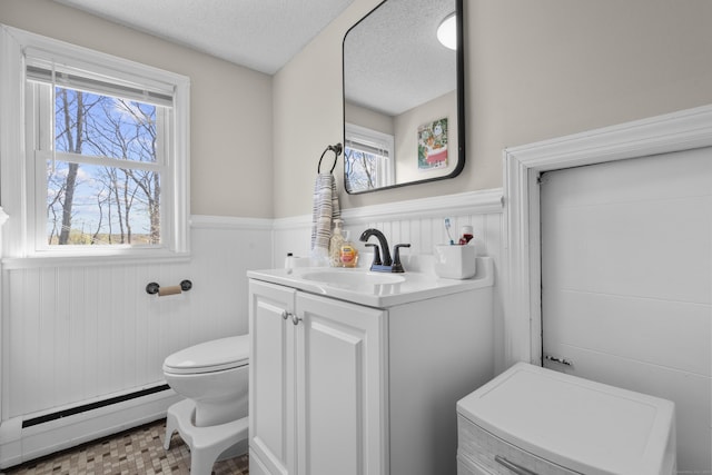 bathroom with baseboard heating, wainscoting, toilet, a textured ceiling, and vanity