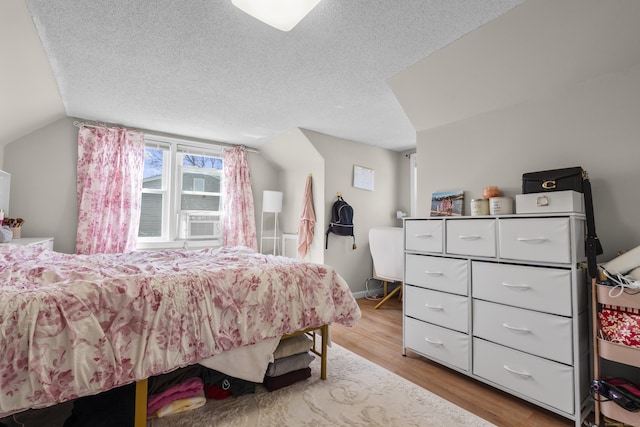 bedroom with a textured ceiling, wood finished floors, vaulted ceiling, and cooling unit