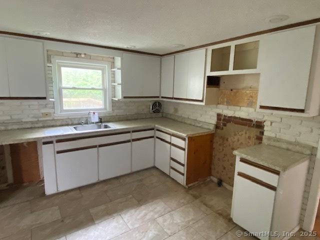 147 Chester St, East Hartford, CT 06108 - kitchen with a sink, decorative backsplash, a textured ceiling, white cabinetry, and light countertops