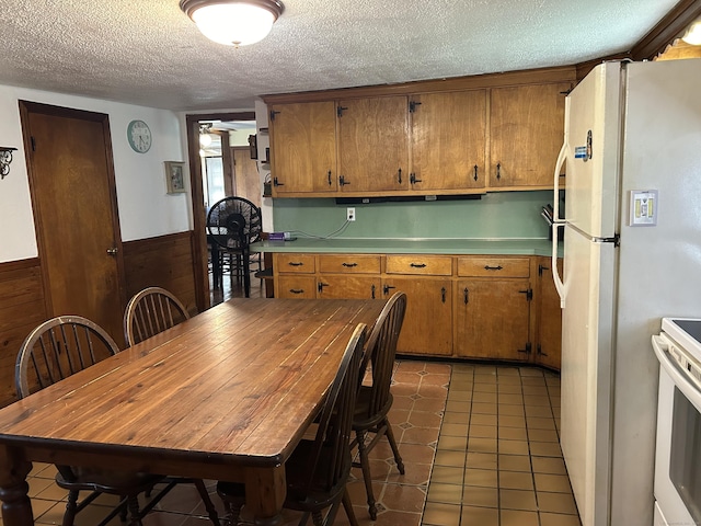 2060 Perkins St, Bristol, CT 06010 - kitchen featuring white appliances, a textured ceiling, brown cabinetry, light tile patterned floors, and light countertops