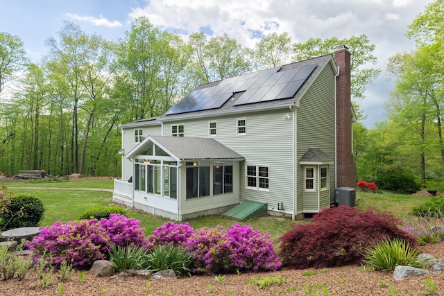 67 Blue Heron Dr, East Hampton, CT 06424 - rear view of house featuring a sunroom, central air condition unit, roof mounted solar panels, a chimney, and a shingled roof
