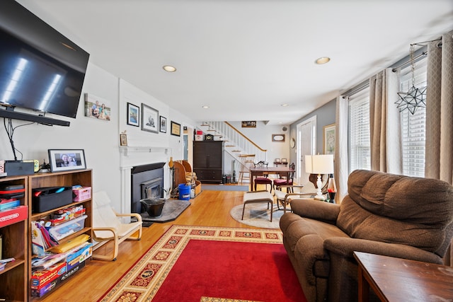 living room with stairs, a fireplace with raised hearth, wood finished floors, and recessed lighting