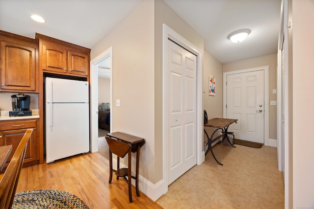 kitchen featuring freestanding refrigerator, brown cabinetry, light countertops, baseboards, and recessed lighting