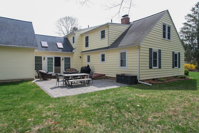 back of house featuring a patio area, a yard, a chimney, and roof with shingles