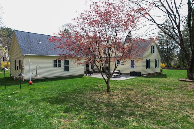 rear view of house with a patio, roof with shingles, and a yard