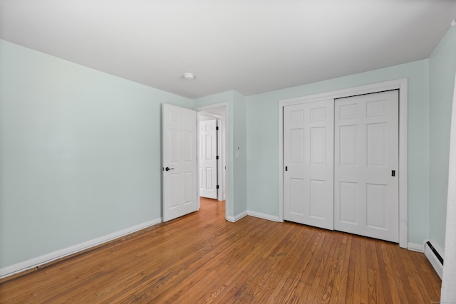 unfurnished bedroom featuring a baseboard heating unit, wood-type flooring, baseboards, and a closet