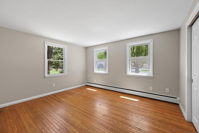 unfurnished room featuring a baseboard heating unit, hardwood / wood-style floors, and baseboards