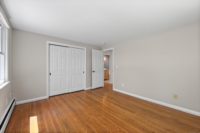 unfurnished bedroom with baseboard heating, hardwood / wood-style flooring, baseboards, and a closet