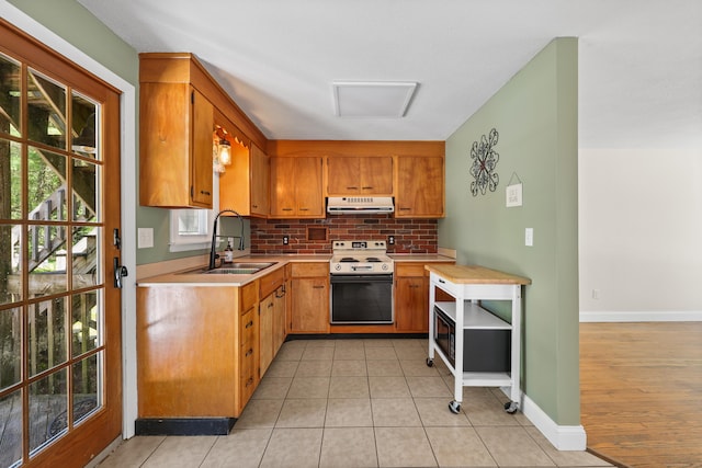 kitchen with electric stove, under cabinet range hood, a sink, backsplash, and light countertops