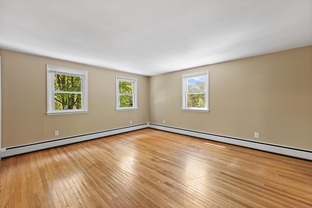 empty room with a baseboard radiator, plenty of natural light, hardwood / wood-style flooring, and baseboards