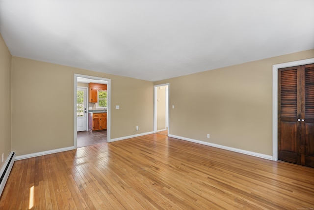 unfurnished living room with baseboards, baseboard heating, and light wood-style floors