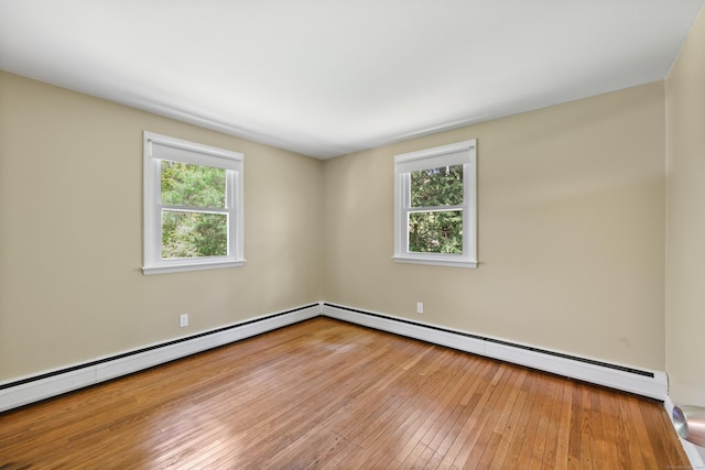 unfurnished room featuring plenty of natural light, hardwood / wood-style floors, and a baseboard heating unit