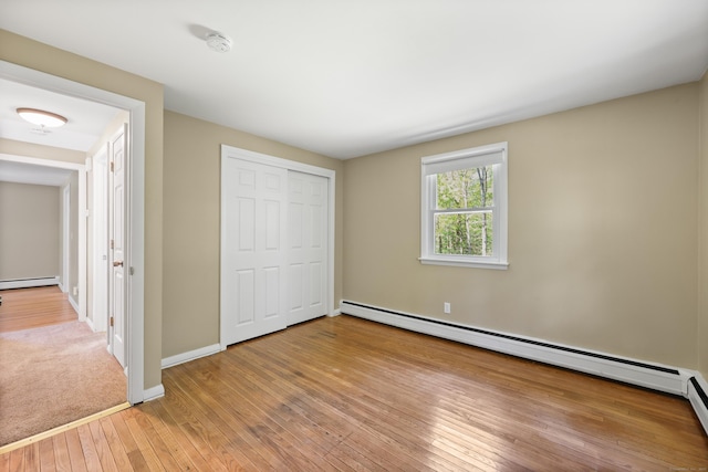 unfurnished bedroom featuring a baseboard radiator, light wood finished floors, a closet, and baseboards