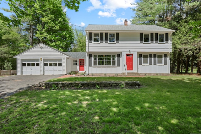 colonial house with a chimney, asphalt driveway, a garage, and a front yard