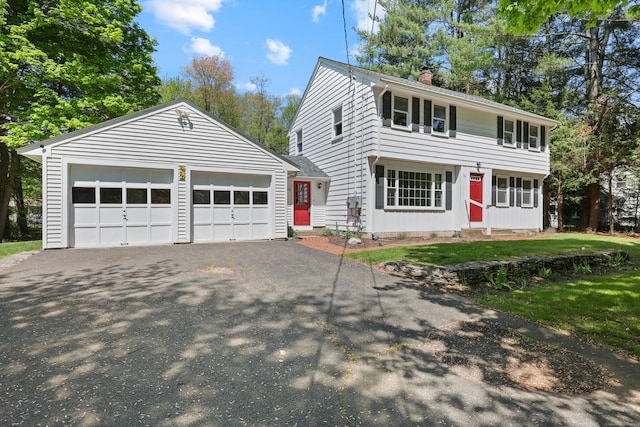 colonial home featuring a chimney, entry steps, and asphalt driveway