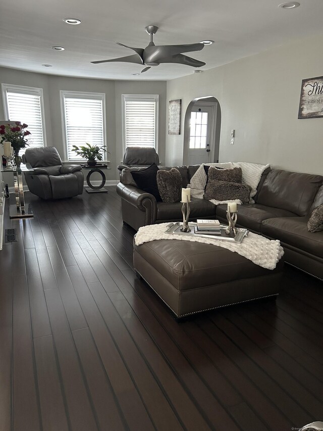 living area with arched walkways, ceiling fan, and dark wood finished floors