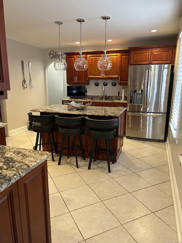 kitchen with stainless steel fridge, light tile patterned floors, a kitchen bar, baseboards, and hanging light fixtures