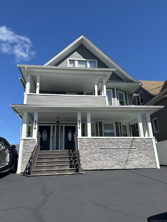 view of front of house with stone siding, a porch, and a balcony