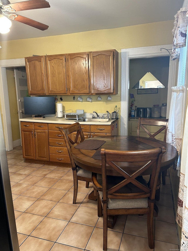 kitchen featuring a sink, light countertops, light tile patterned floors, brown cabinetry, and a ceiling fan