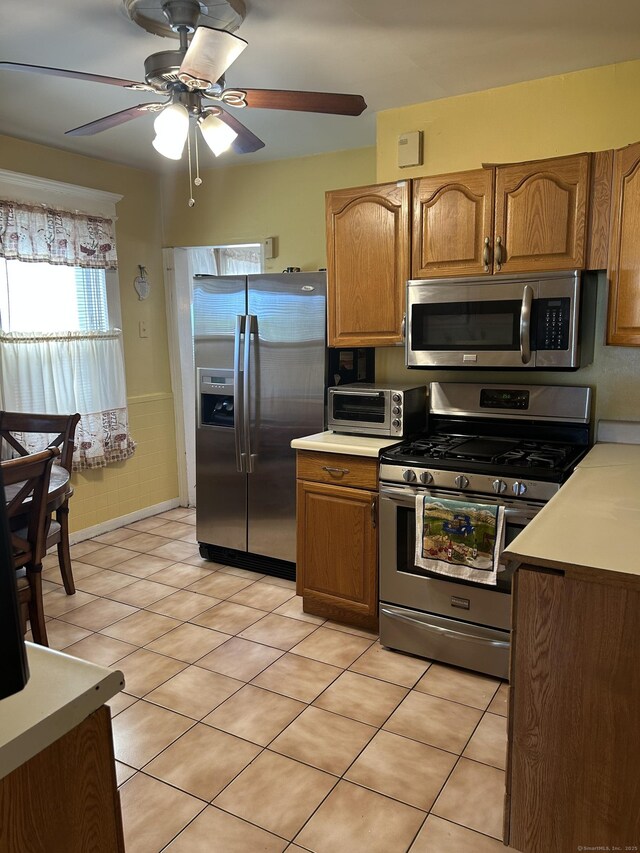 kitchen with appliances with stainless steel finishes, a ceiling fan, brown cabinetry, and light countertops