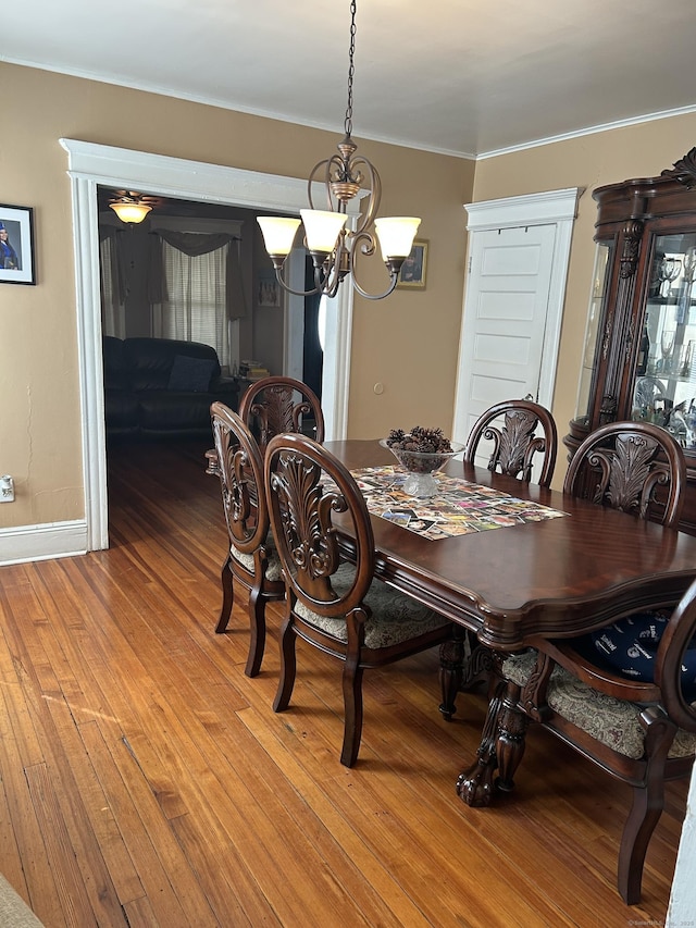 dining space with a chandelier, ornamental molding, light wood-style flooring, and baseboards