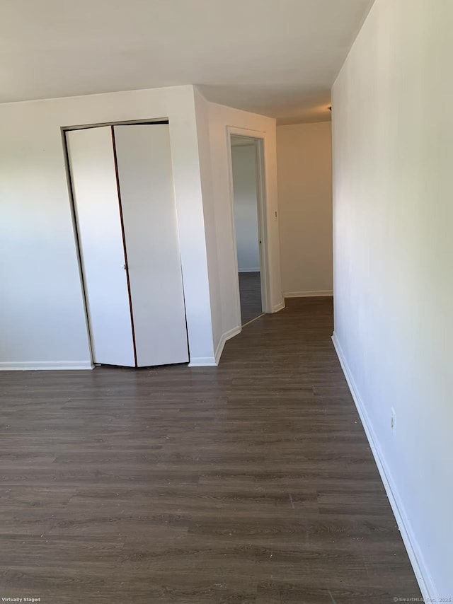 unfurnished bedroom featuring baseboards, a closet, and dark wood-style flooring