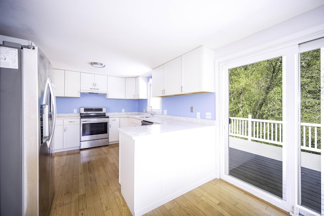 kitchen featuring appliances with stainless steel finishes, a peninsula, light countertops, a sink, and light wood finished floors